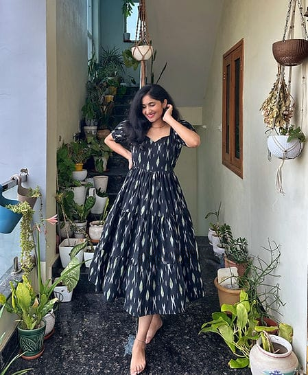 Woman wearing black cotton middi gown for women with white patterns posing in a plant-filled corridor