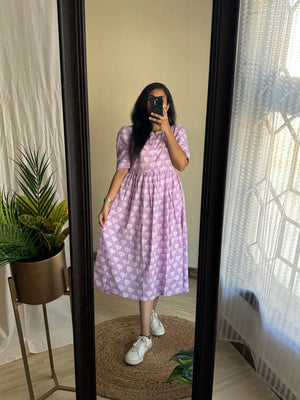 Woman wearing a lavender printed full flair middy gown for women with white sneakers standing in front of a mirror