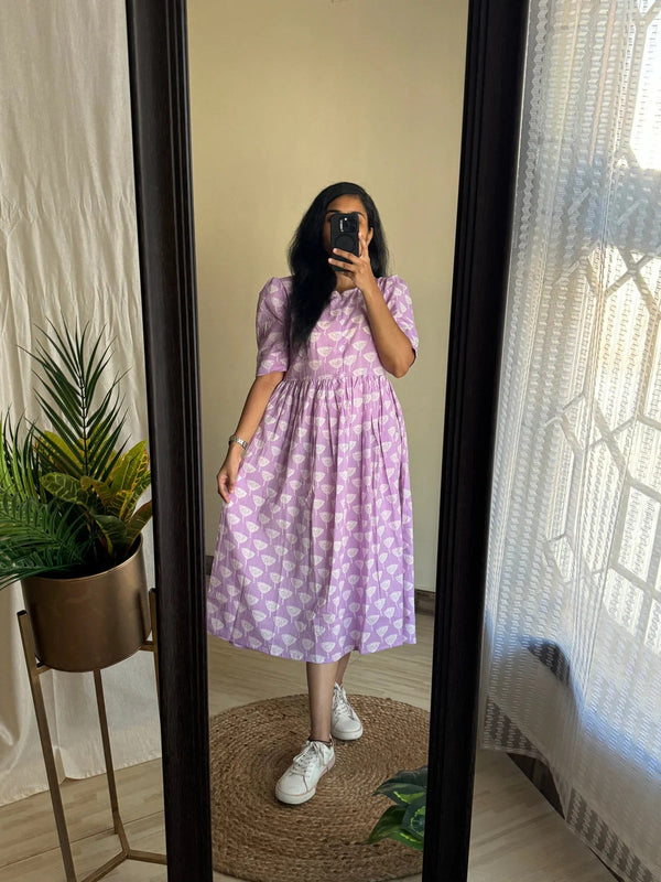 Woman wearing a lavender printed full flair middy gown for women with white sneakers standing in front of a mirror