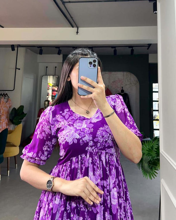 Woman wearing purple floral flowy maternity gown taking mirror selfie indoors