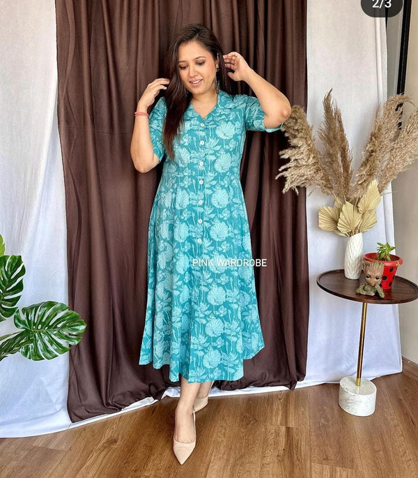 Woman wearing a blue floral cotton dress by Cotton Suit against a brown curtain backdrop
