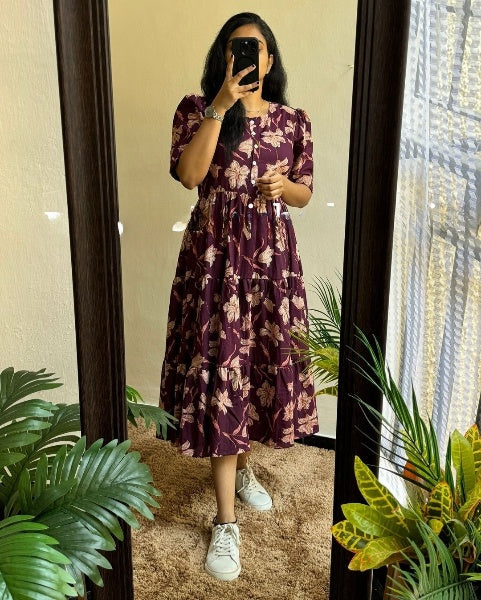 Woman wearing a purple floral maxi dress with sleeves standing in front of a mirror with green plants around
