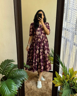 Woman wearing a purple floral maxi dress with sleeves standing in front of a mirror indoors