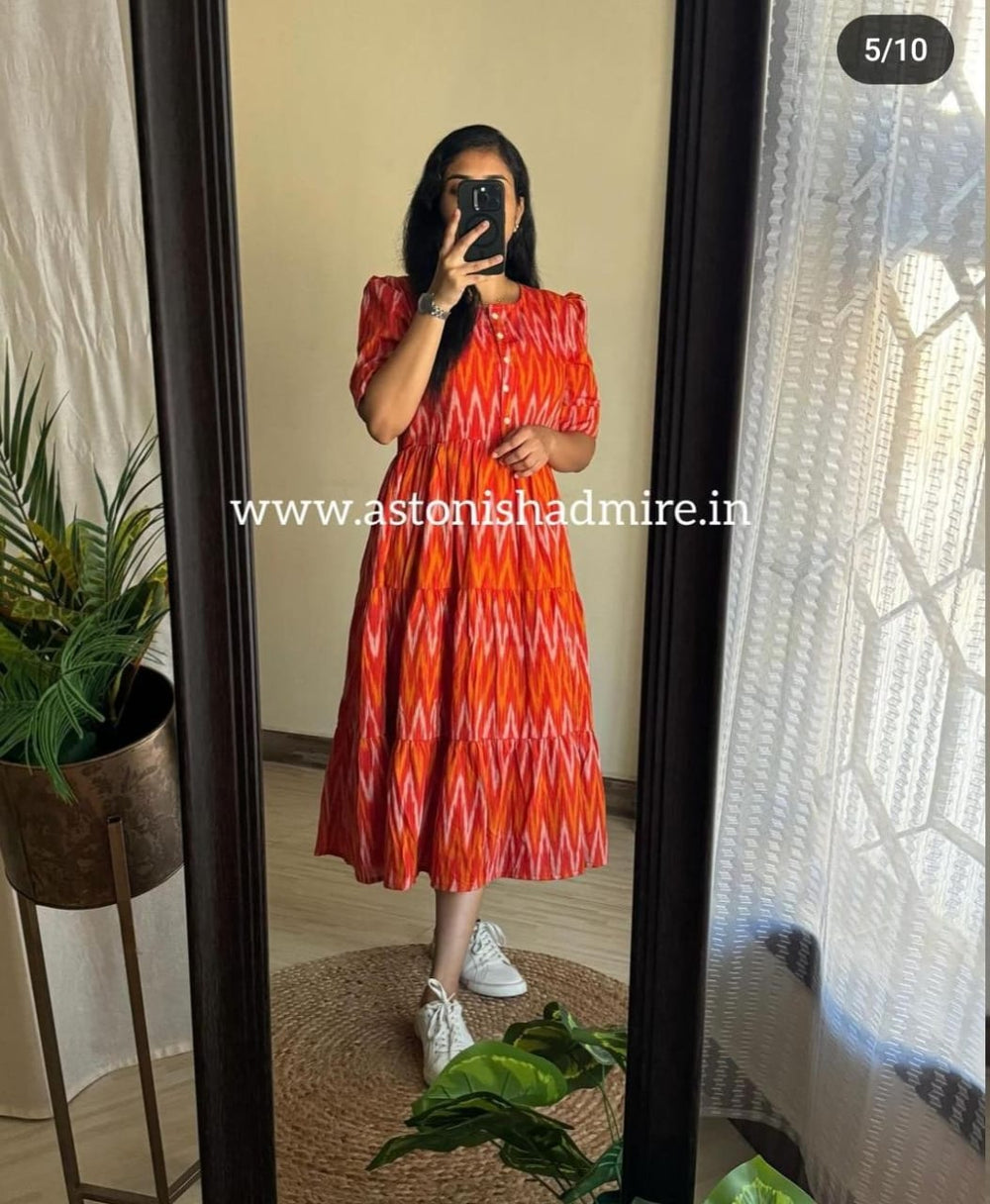 Woman wearing a rust orange ikkat middy gown with short sleeves and white sneakers standing in front of a mirror
