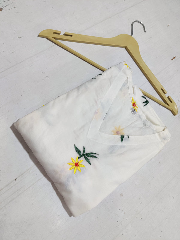 Folded white cotton embroidered midi dress with yellow floral design by  Cotton Suit on beige hanger