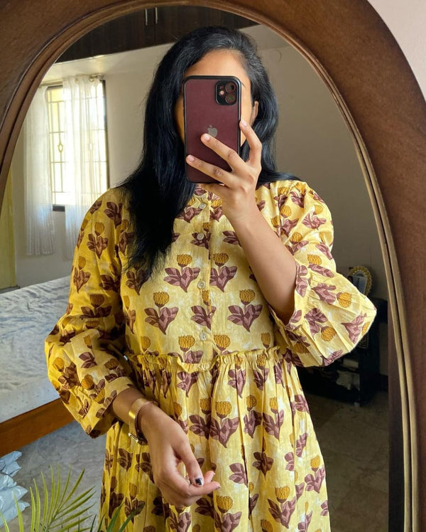 Woman wearing a women's flower print midi dress in yellow with brown floral design taking a mirror selfie