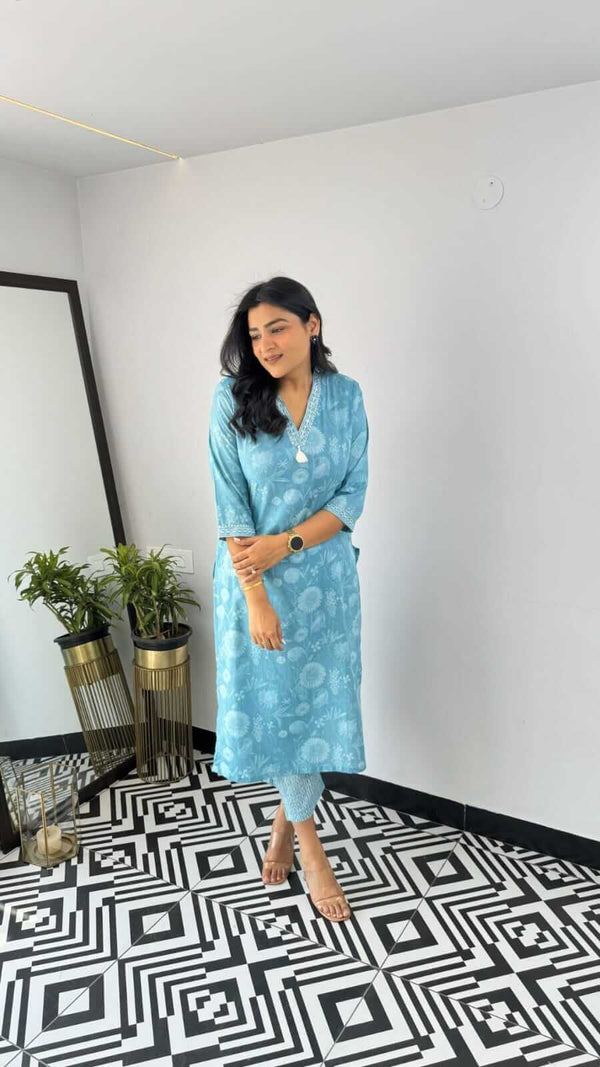 Woman wearing a yellow and pink office wear kurta in blue floral design standing inside a modern room