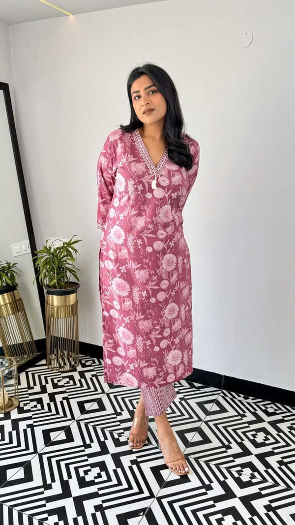 Woman wearing pink floral kurta with matching pants standing in a modern room with patterned floor